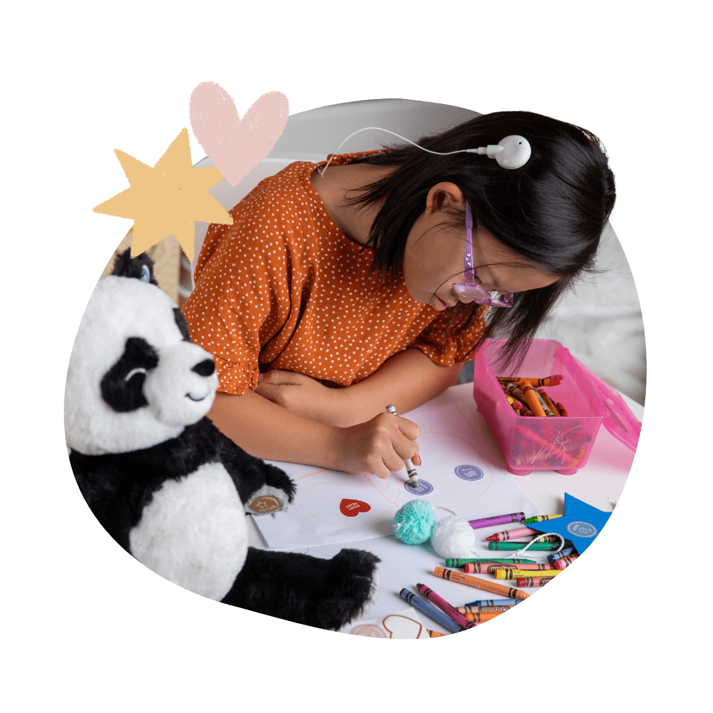 Little girl with hearing aid and glasses coloring with Pause with Panda